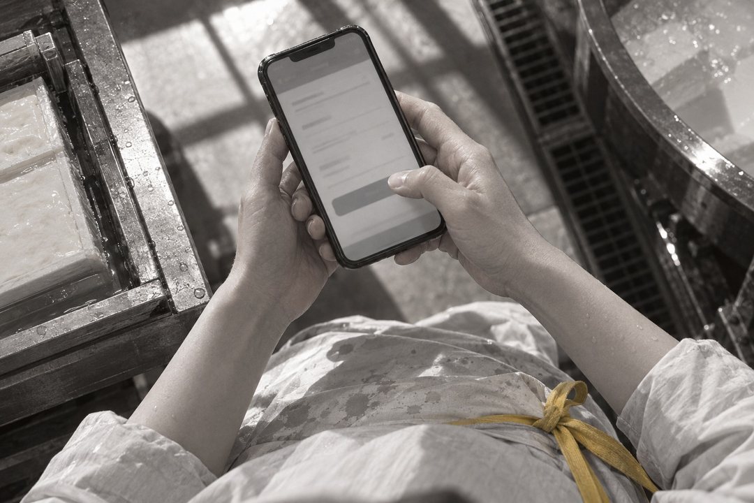 寄り。真琴の親指が、スマホの振込の画面の確定のボタンの上で止まる。画面の字は読めない。濡れた前掛け。